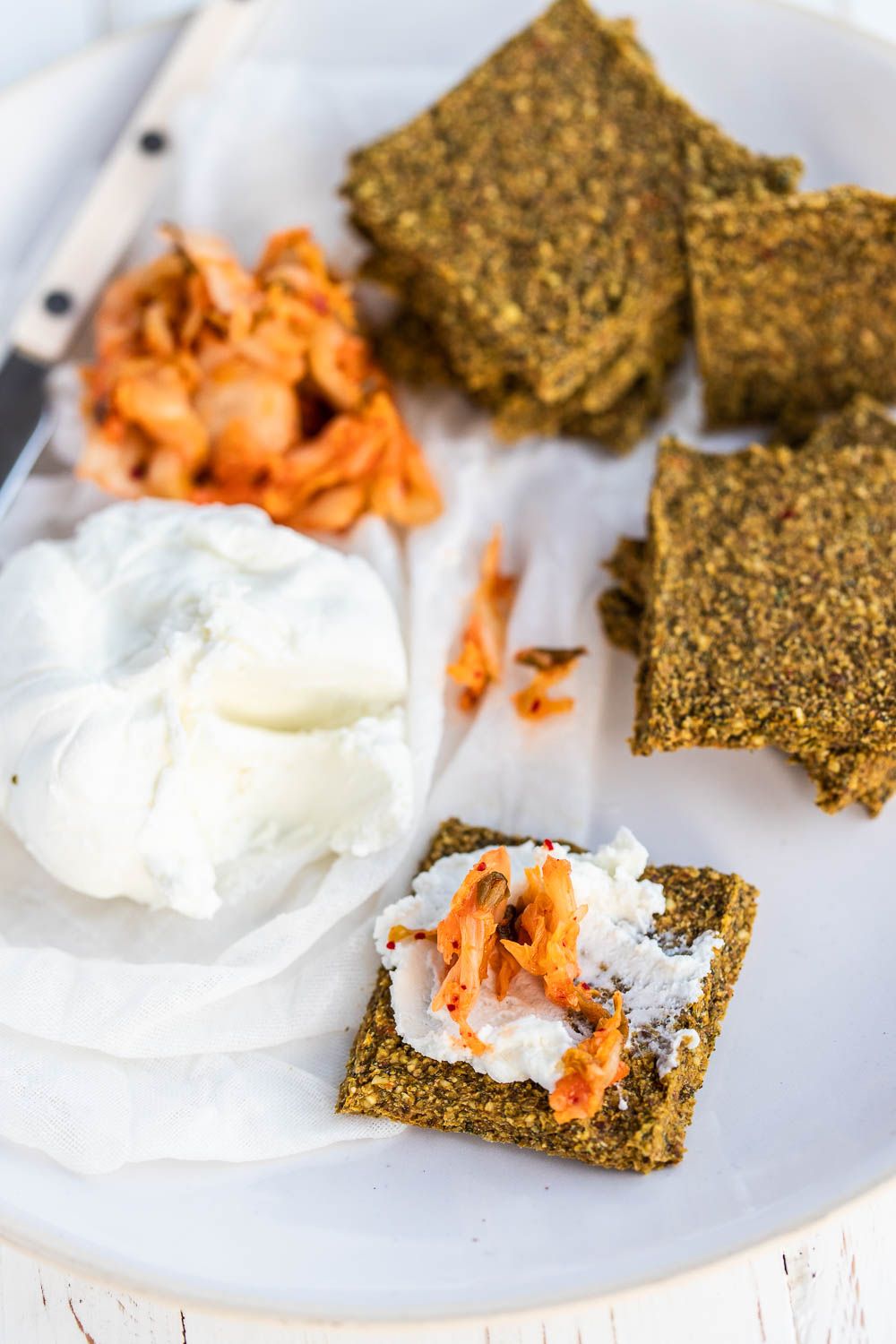 kimchi kale crackers topped with nut cheese and kimchi on a white background