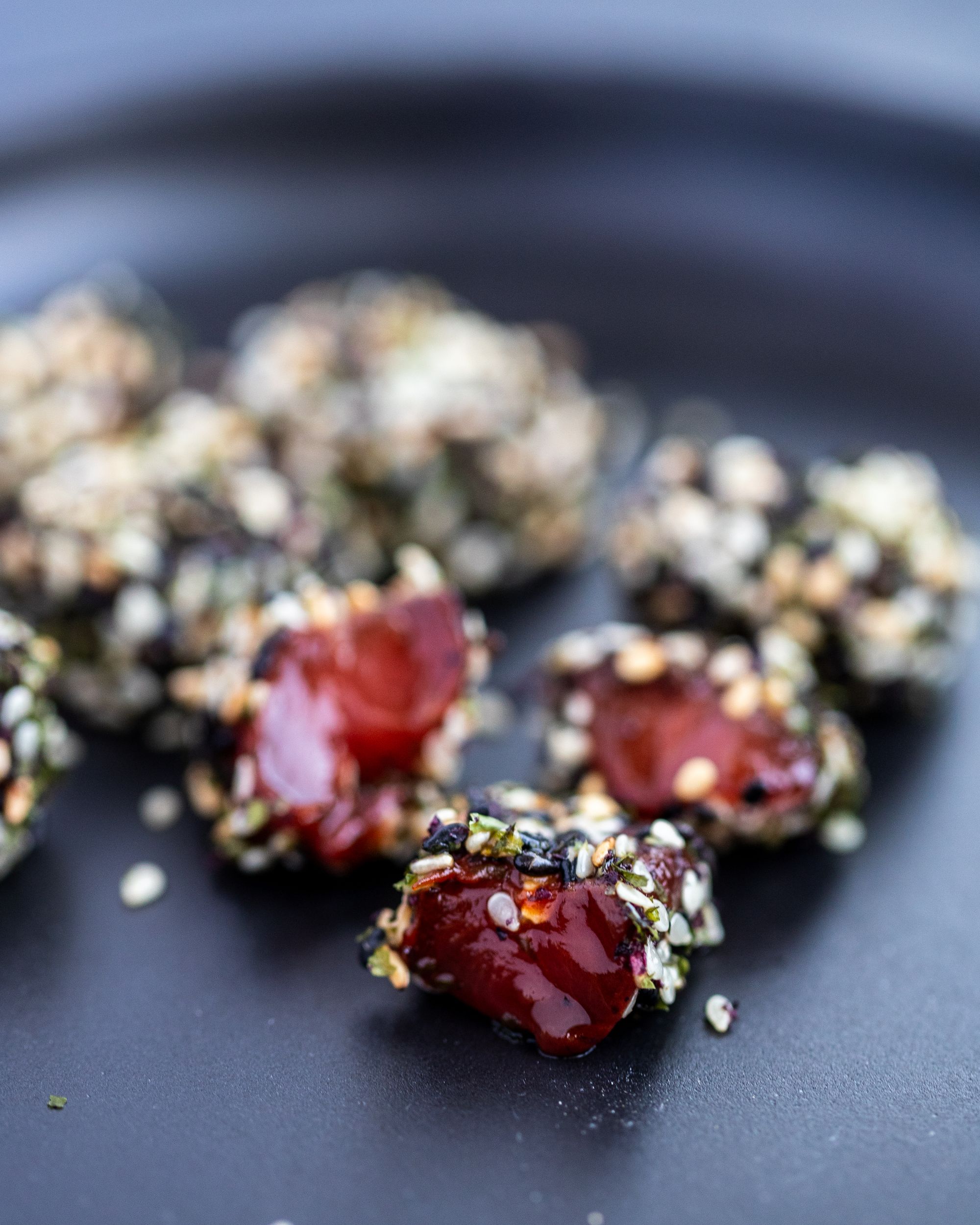 Pieces of raw vegan watermelon tuna done in the dehydrator, covered in sesame seed on a black plate