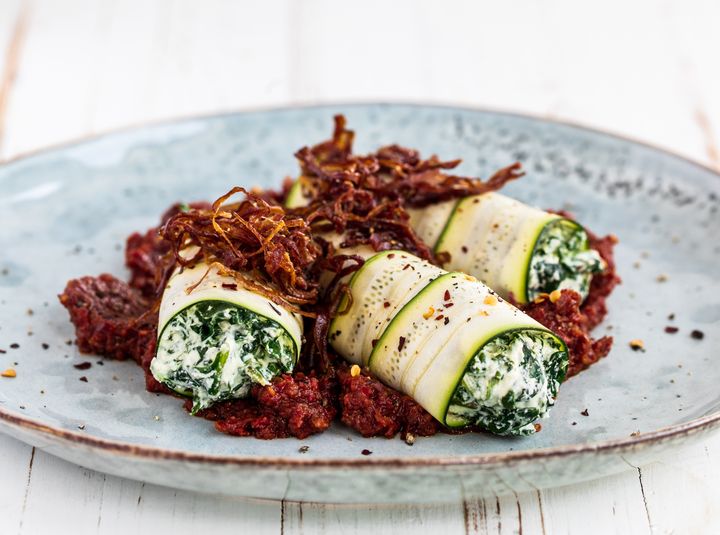 Blue plate of raw vegan spinach macadamia ricotta cannelloni on a white background