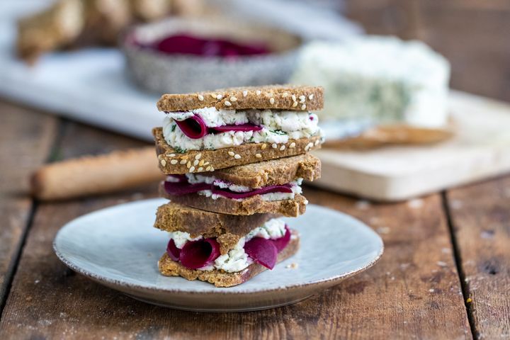 Raw vegan fermented bread sandwiches filled with macadamia cheese and fermented beetroot on a blue plate and wooden table