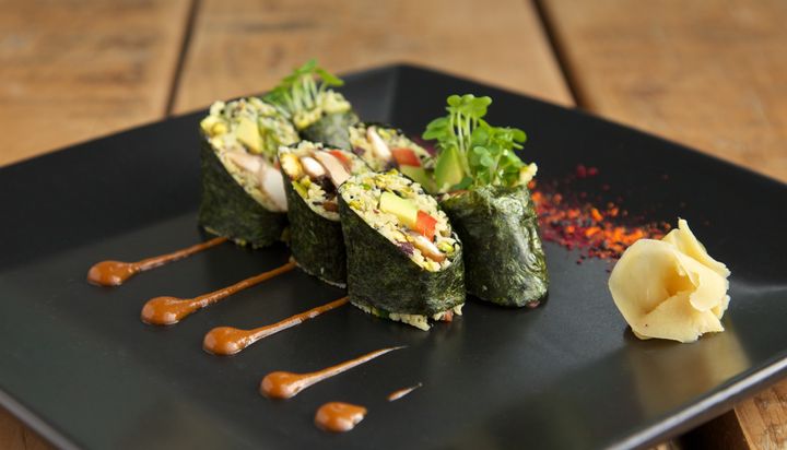 A black plate of raw vegan sushi with pickled ginger and miso sauce on a wooden table
