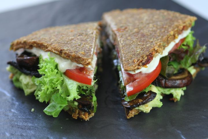 Raw vegan zucchini bread sandwich with cashew mayo, avocado, lettuce and tomatoes on a slate.