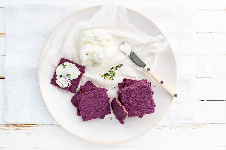 Sauerkraut crackers with macadamia cheese on a white plate with a knife and napkin on a white table