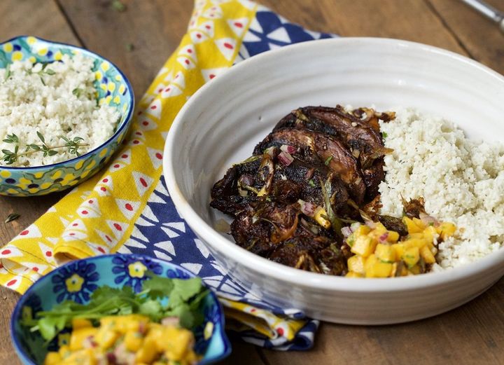 Jerk spiced portobello mushrooms with coconut cauliflower rice and mango salsa in a white bowl on a wooden background