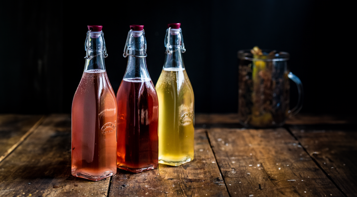 Three bottles of fizzy water kefir in different flavours on a wooden background