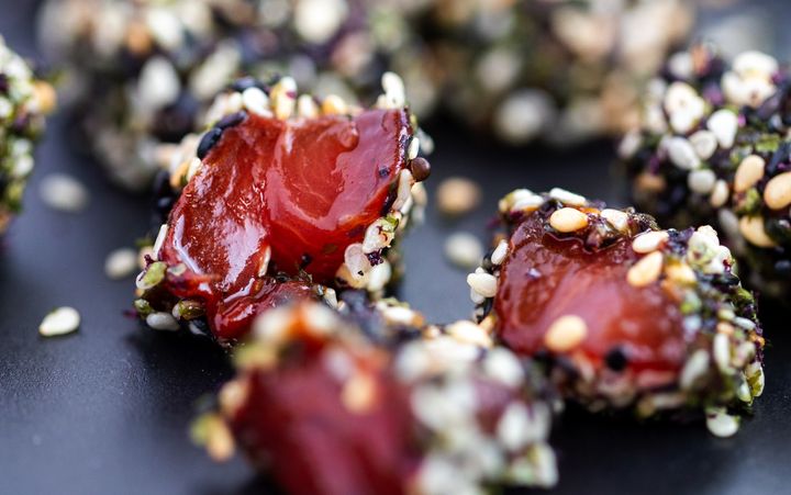 Pieces of watermelon tuna covered in sesame seed on a black plate