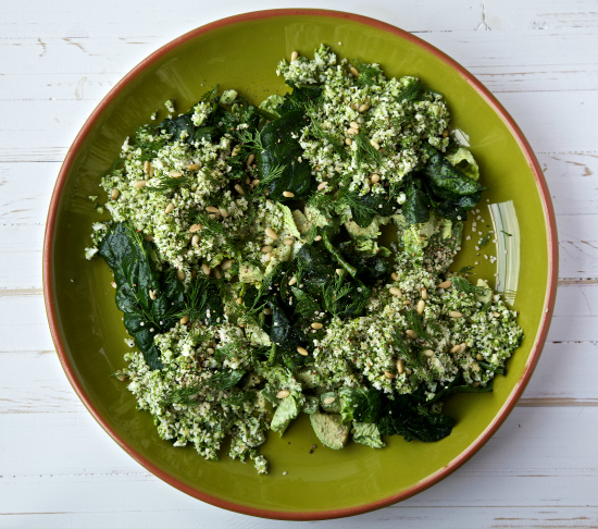 Overhead shot of a green goddess salad on a green plate and white wooden background