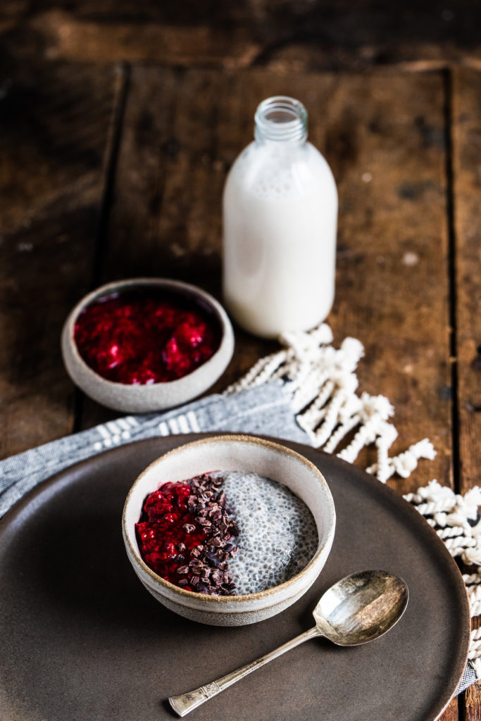 Vanilla chia pudding in a white bowl with cacao nibs and raspberry jam