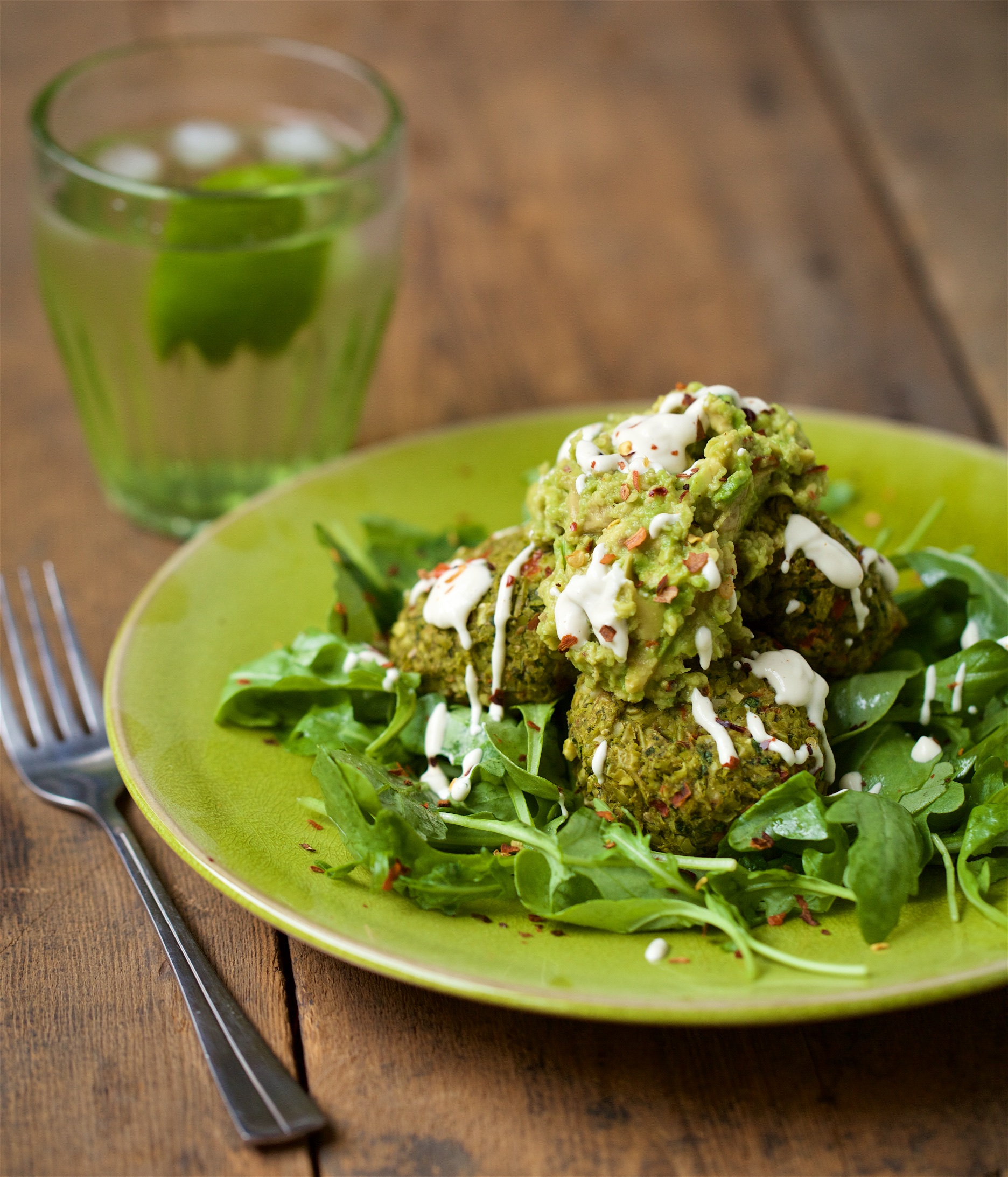 Pea and mint croquettes with guacamole and cashew sour cream on spinach on  green plate