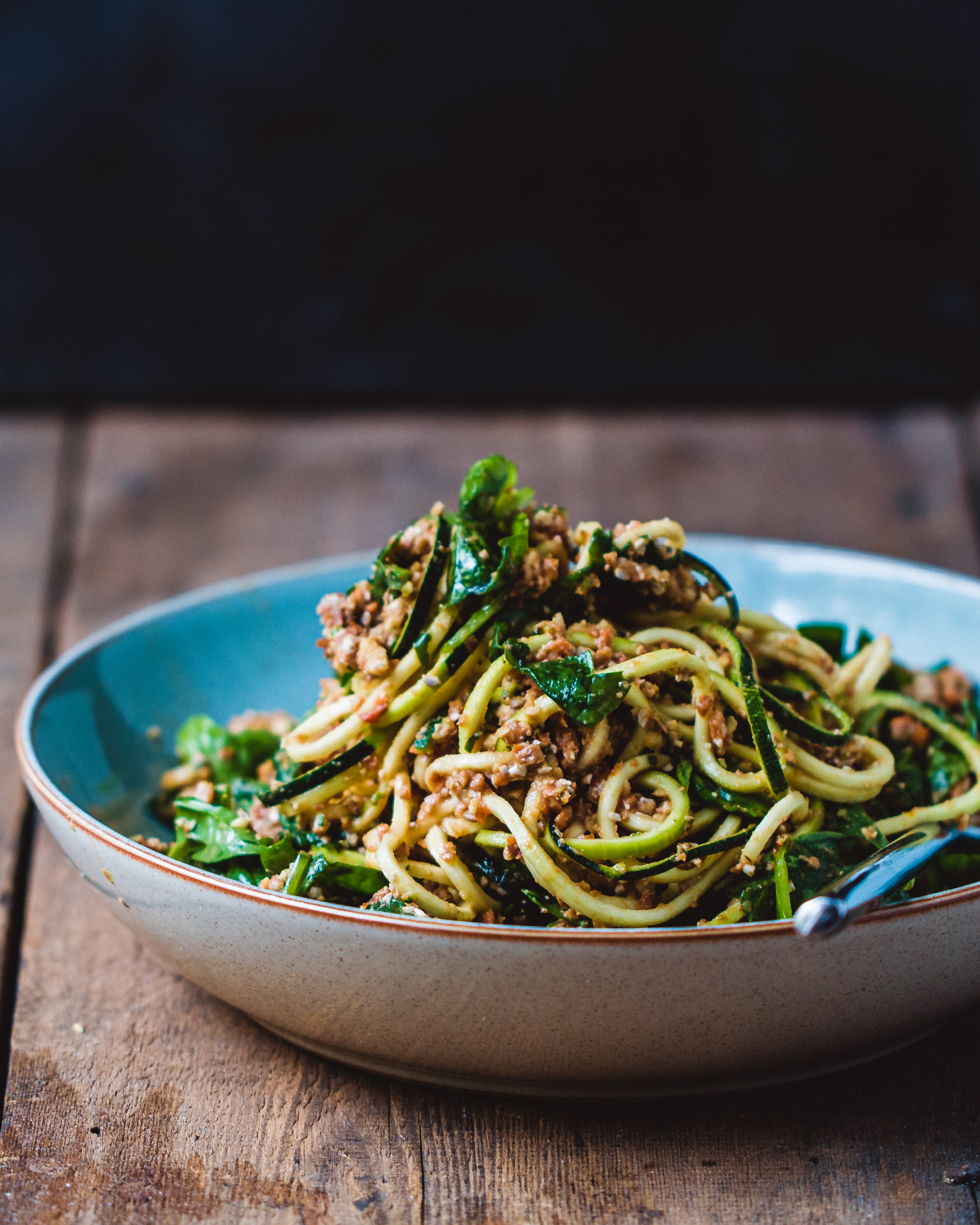 Raw vegan zucchini spaghetti bolognese in a blue and white bowl on a wooden surface