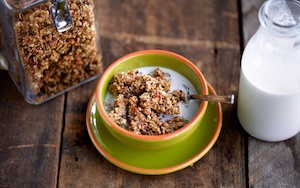 Hemp granola with almond milk in a green bowl on a wooden background
