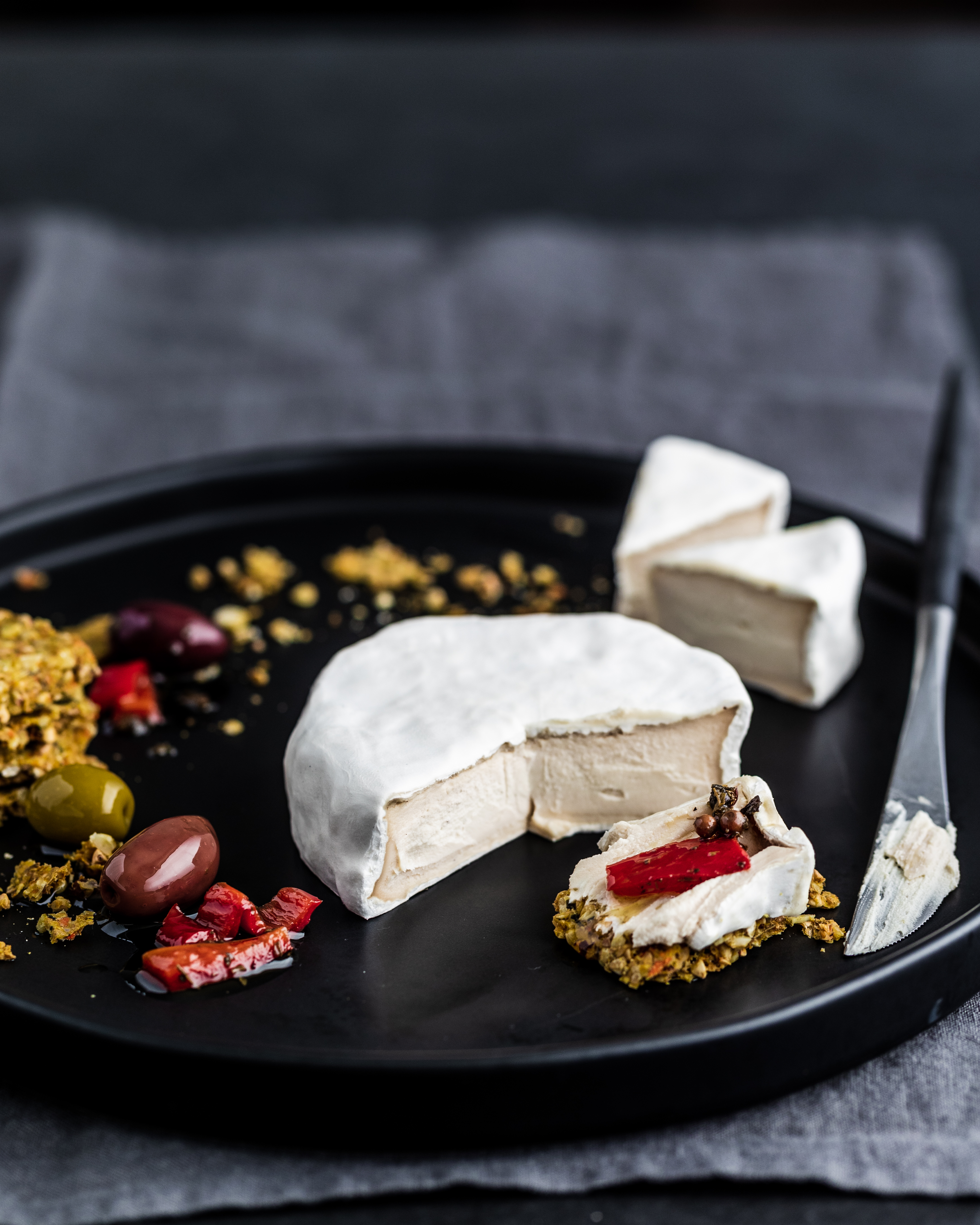 cashew nut camembert cheese on a black plate with crackers, olive and red peppers