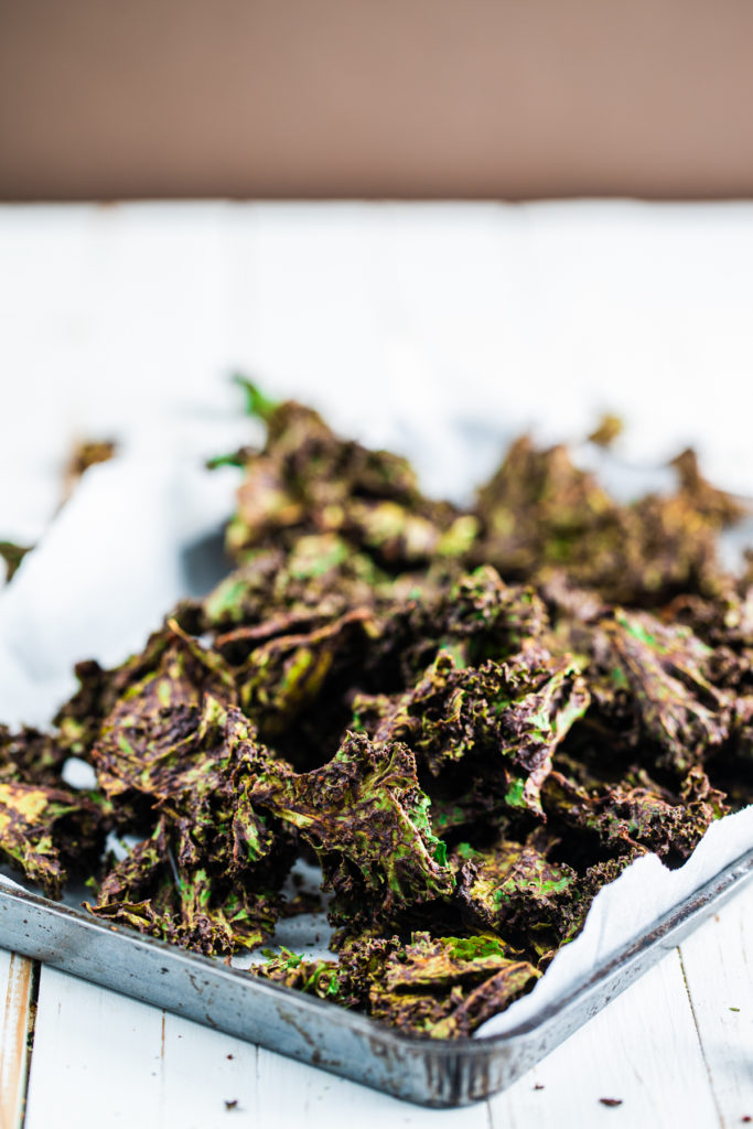 Raw dehydrated kale chips in a baking pan on a white background