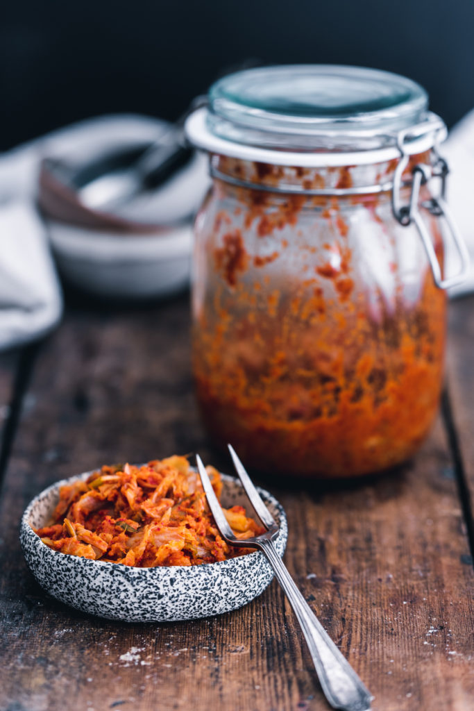 Vegan kimchi in a bowl, with a jar of kimchi behind on a wooden suface