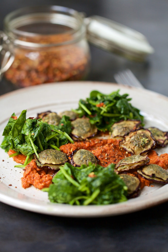 The Aubergine Macadamia Pesto Ravioli is serve on a white plate on top of a gray background