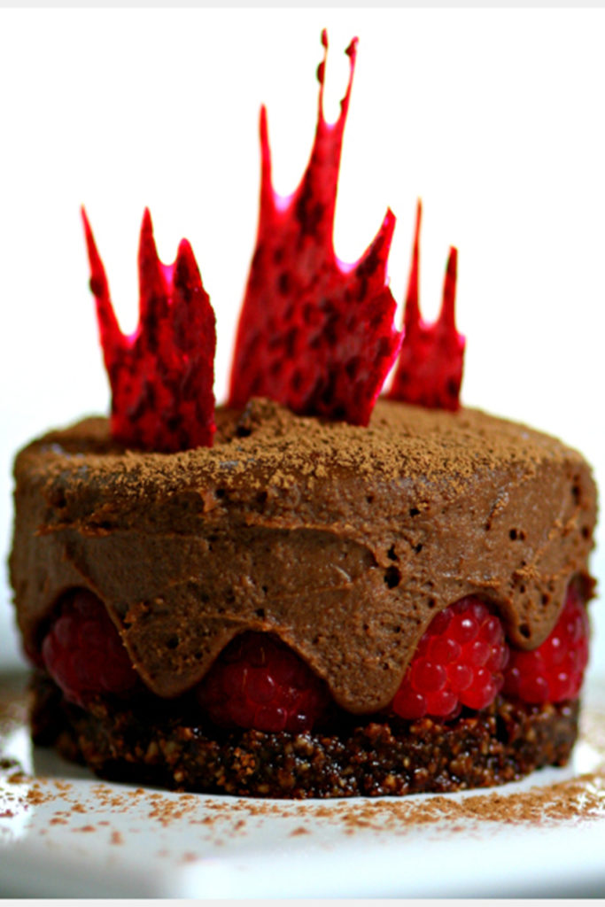 The Chocolate Raspberry Cake with Ginger Chocolate Mousse is dusted with cacao powder on top of a white table
