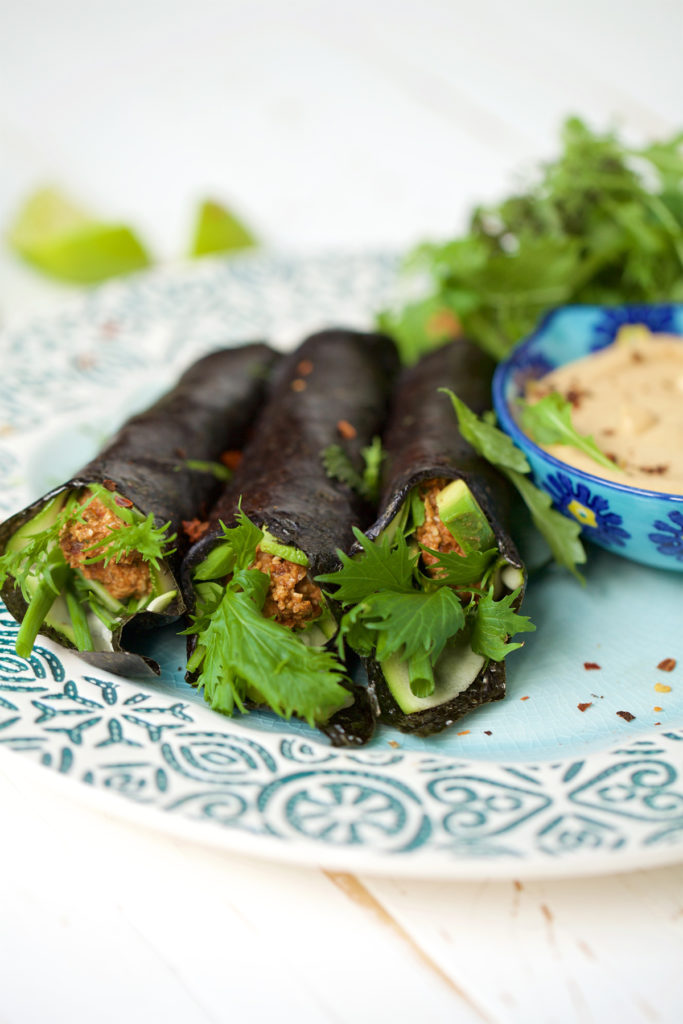 There are three pieces of Nori Taquitos on an elegant place with a few salad leaves on the side and the cashew dip.