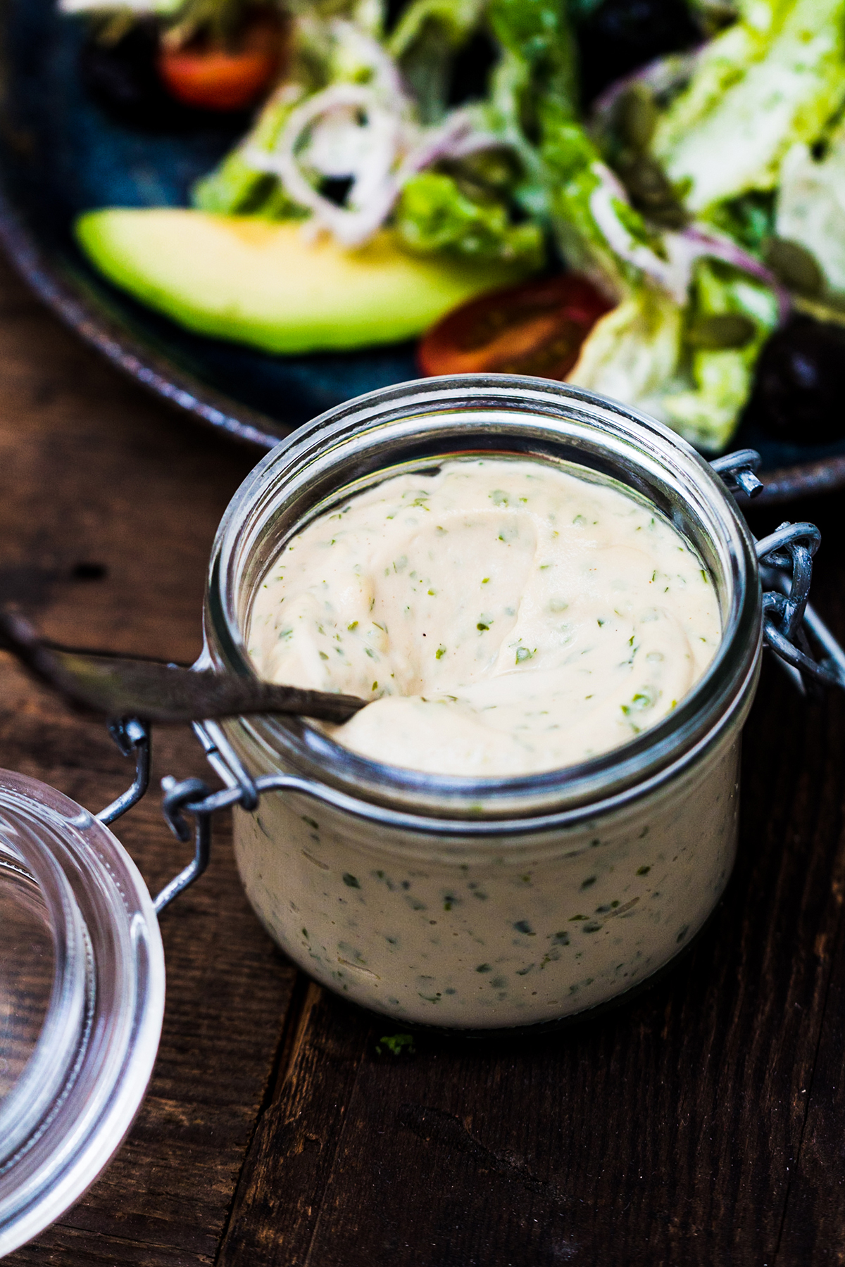 The Caesar dressing is inside a glass fermenting jar on a wooden table.