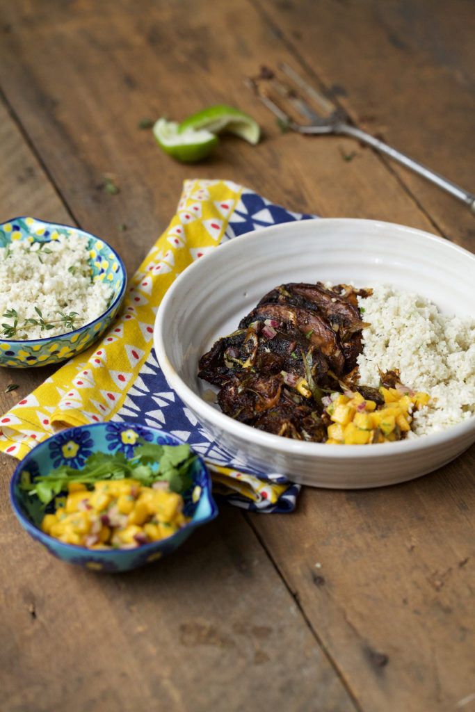 The dish is served on a white bowl on top of a colorful table napkin with some additional mango salsa and cauliflower coconut rice served on the side.