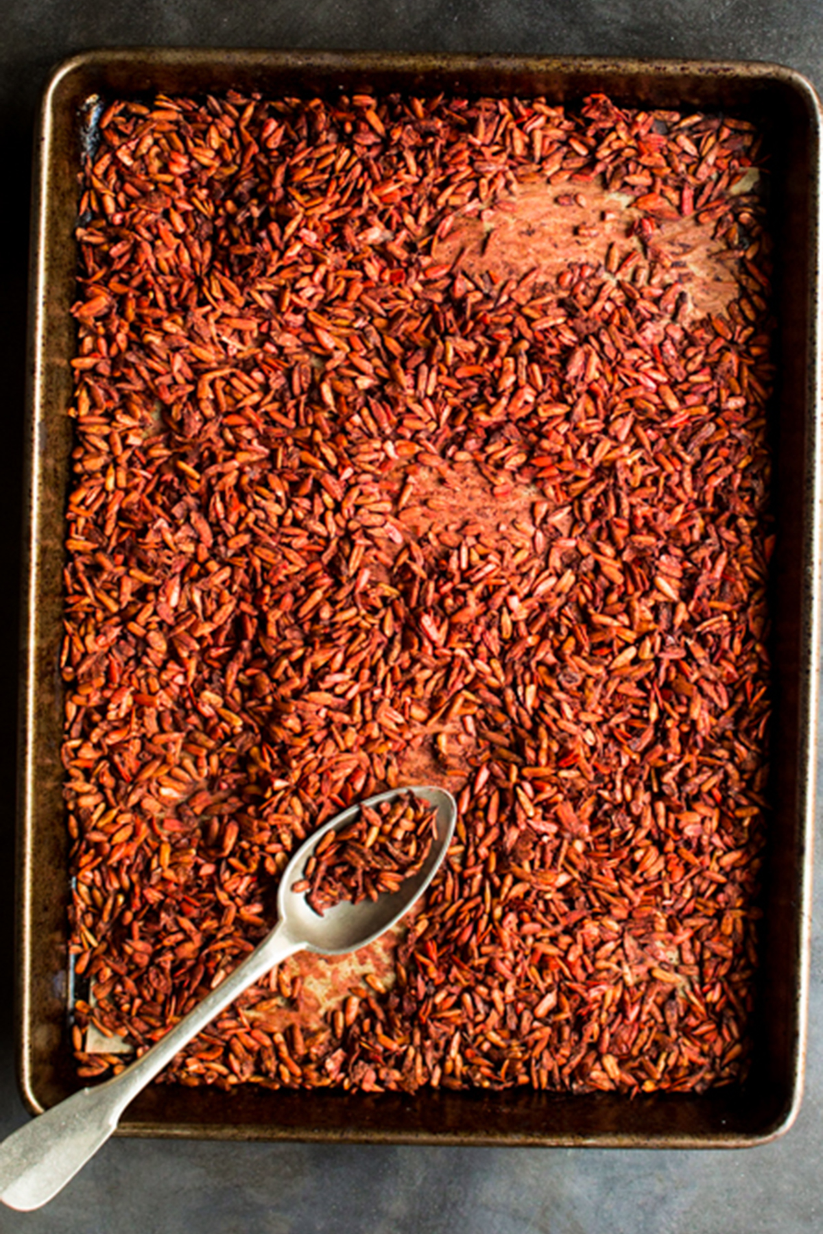 Jerk spiced sunflower seeds on a black baking tray with a silver spoon