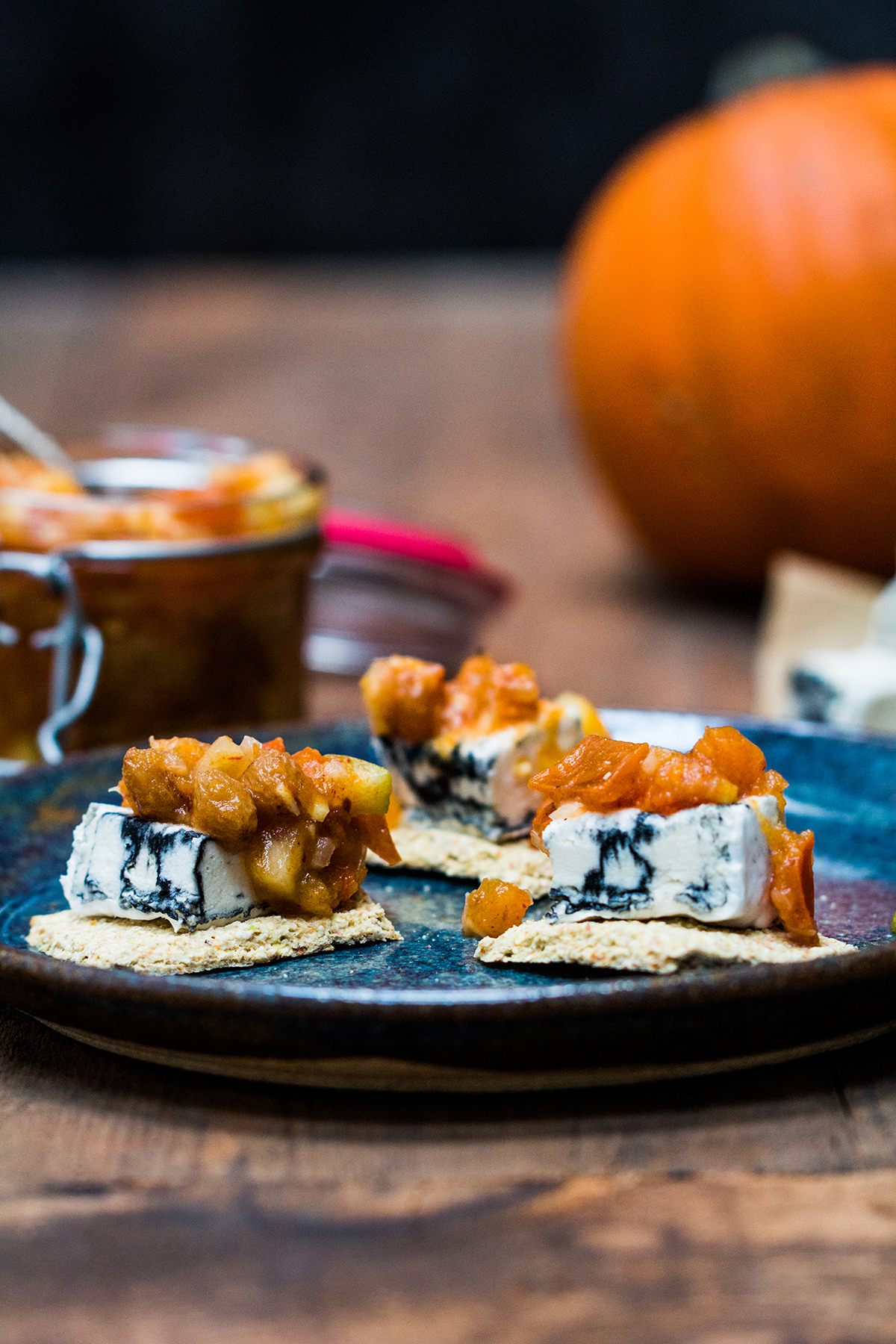 The Persimmon chutney is served as a topping for a tree nut cheese with vegan cracker. The dish is served on a blue plate.