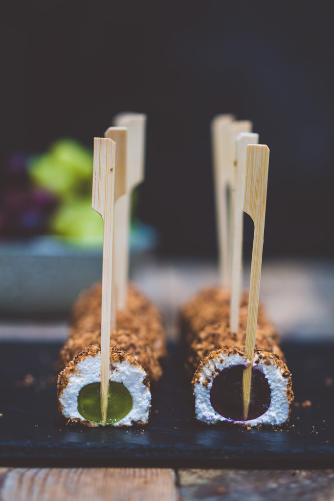 The grape cheese balls are plug with a stick and served on a black rectangular plate.