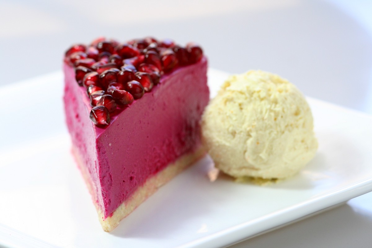 Raw pomegranate cheesecake with clementine gelato on a white plate