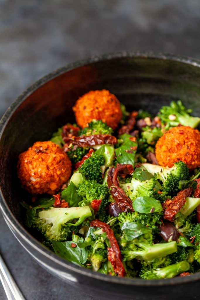 Sundried tomato and broccoli salad in a black bowl on a black background