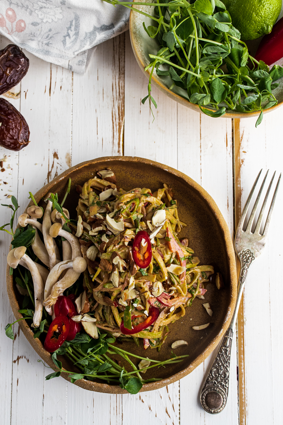 Raw pad Thai in a brown bowl on a white background with a fork