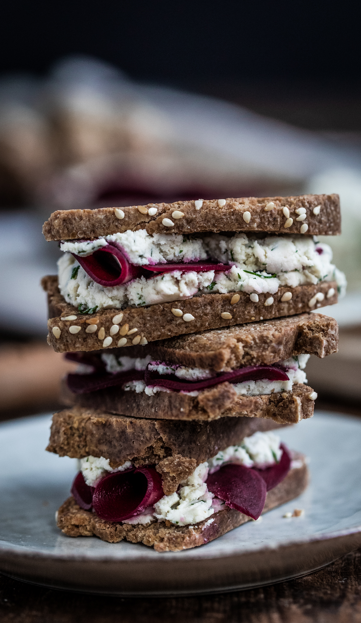 Fermented raw vegan bread made into sandwiches with macadamia cheese and beet slices, stacked up on a blue plate