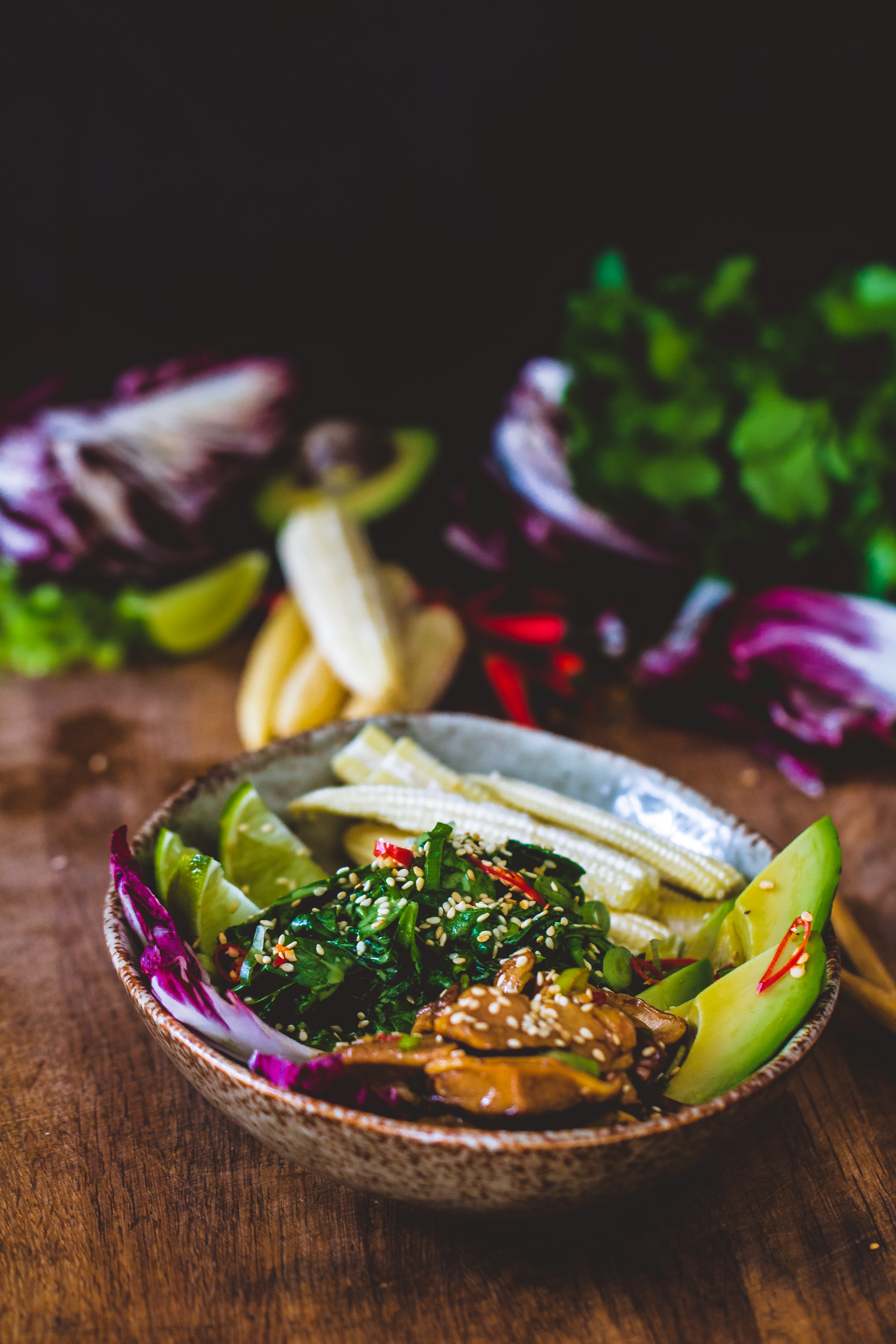 Asian peanut salad dressing on a chopped asian salad in a bowl on a wooden surface with vegetables in the background