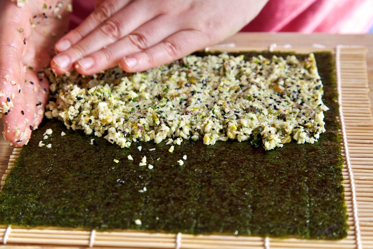 Parsnip rice being spread on top of a nori sheet, on a bamboo rolling mat