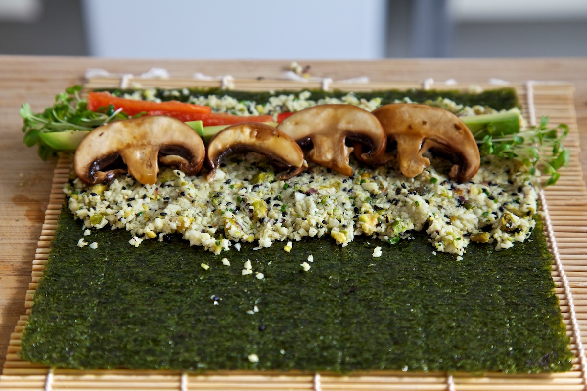 Raw vegan sushi with parsnip rice on a nori sheet, ready to roll on a bamboo mat