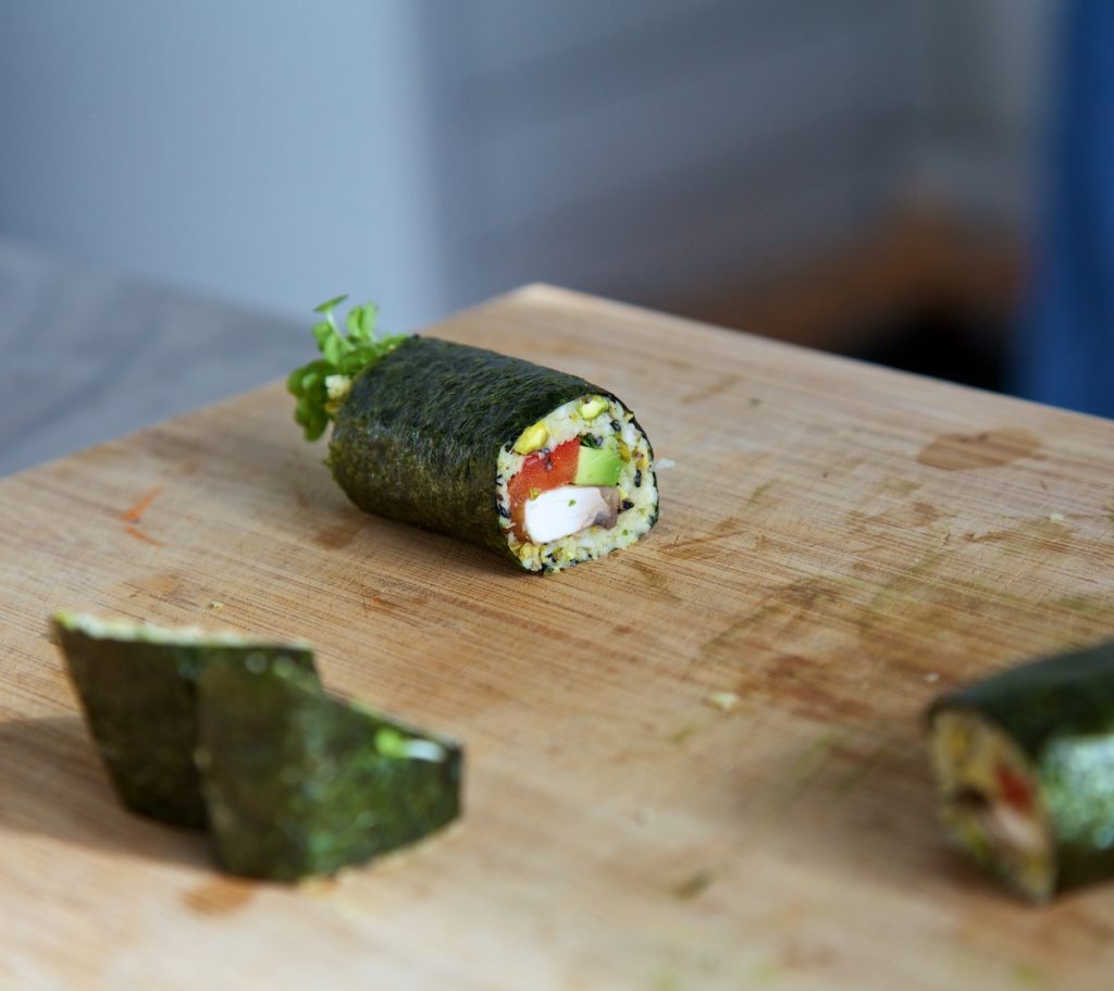 Raw vegan sushi cut into pieces on a wooden chopping board, with one piece laying down showing a cross section of the filling
