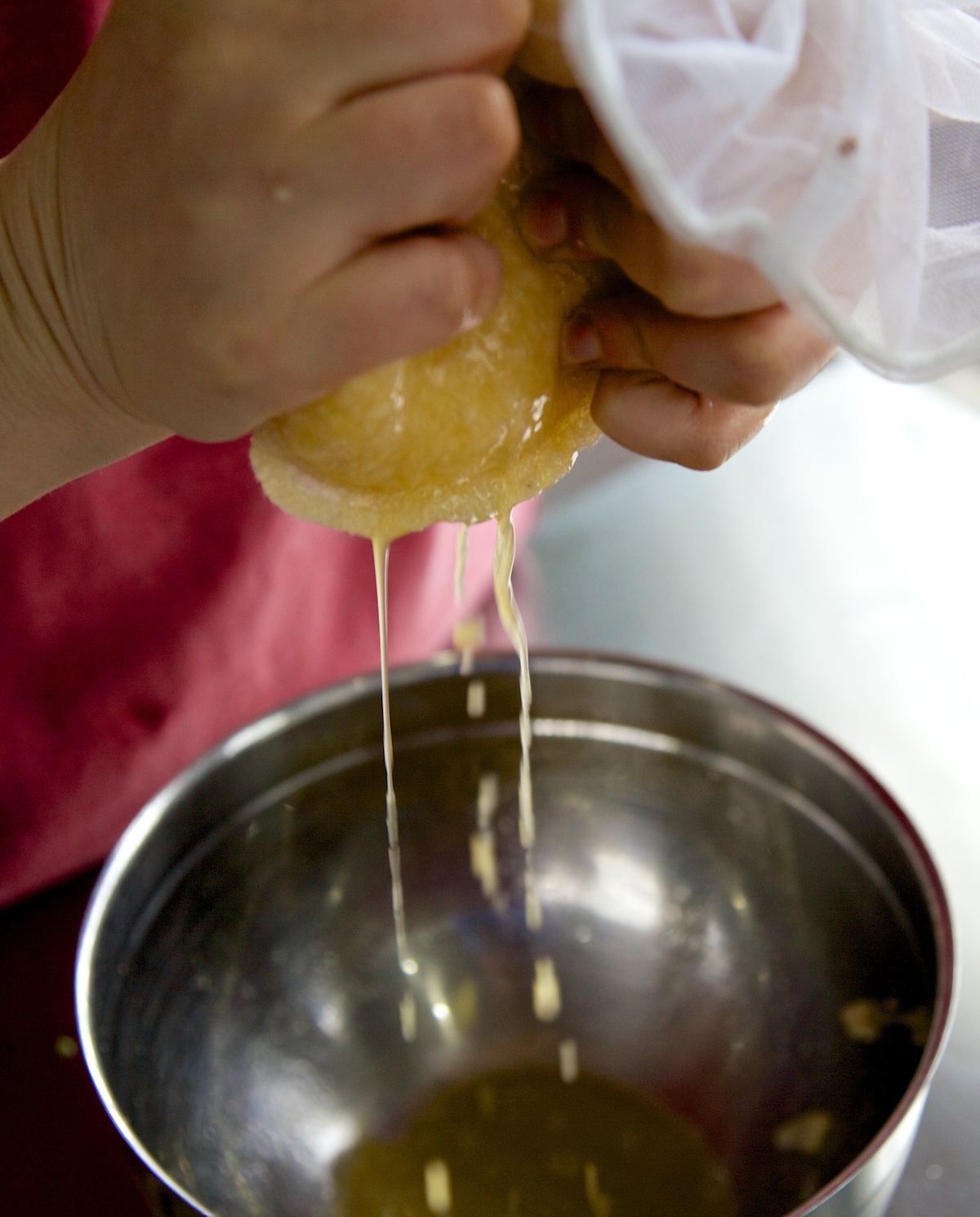 Excess liquid being squeezed out of swede rice in a nut milk bag, over a silver bowl