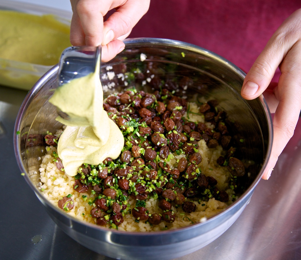 Curried cashew mixture being added to the rest of the swede risotto ingredients in a silver bowl