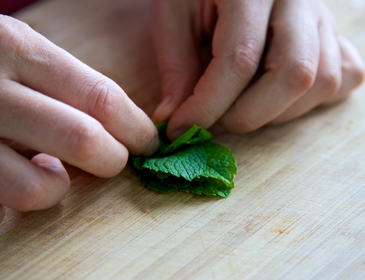 Mint leaves being rolled up on a bamboo chopping board, ready to be cut