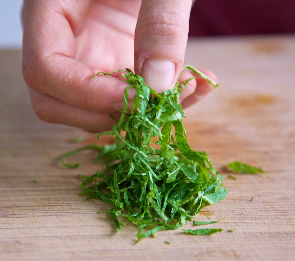 Mint chiffonade being handled on a bamboo chopping board