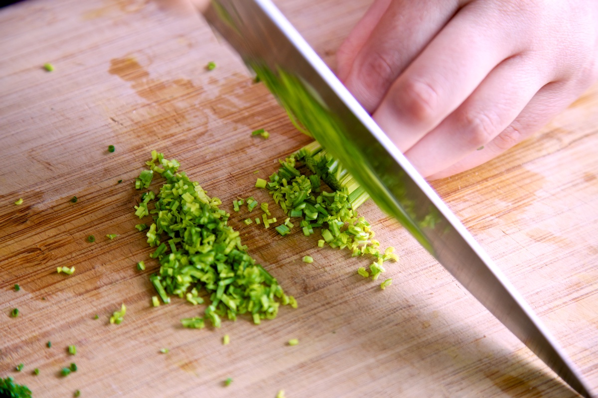 Leeks being cut finely on a bamboo chopping board