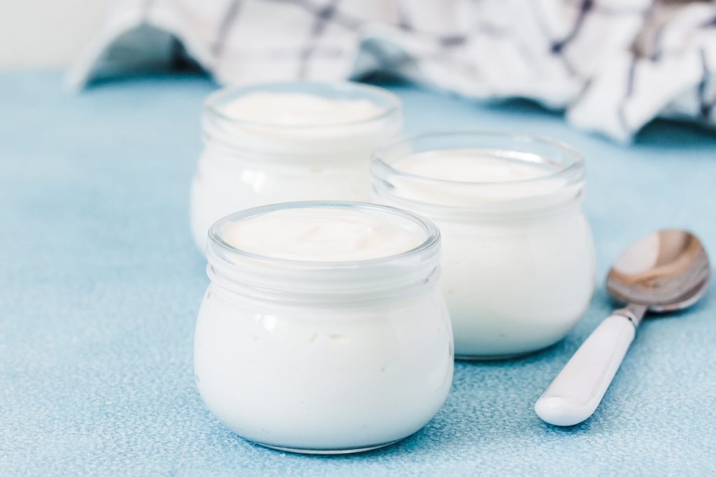 3 jars of coconut yoghurt with a spoon, on a blue surface