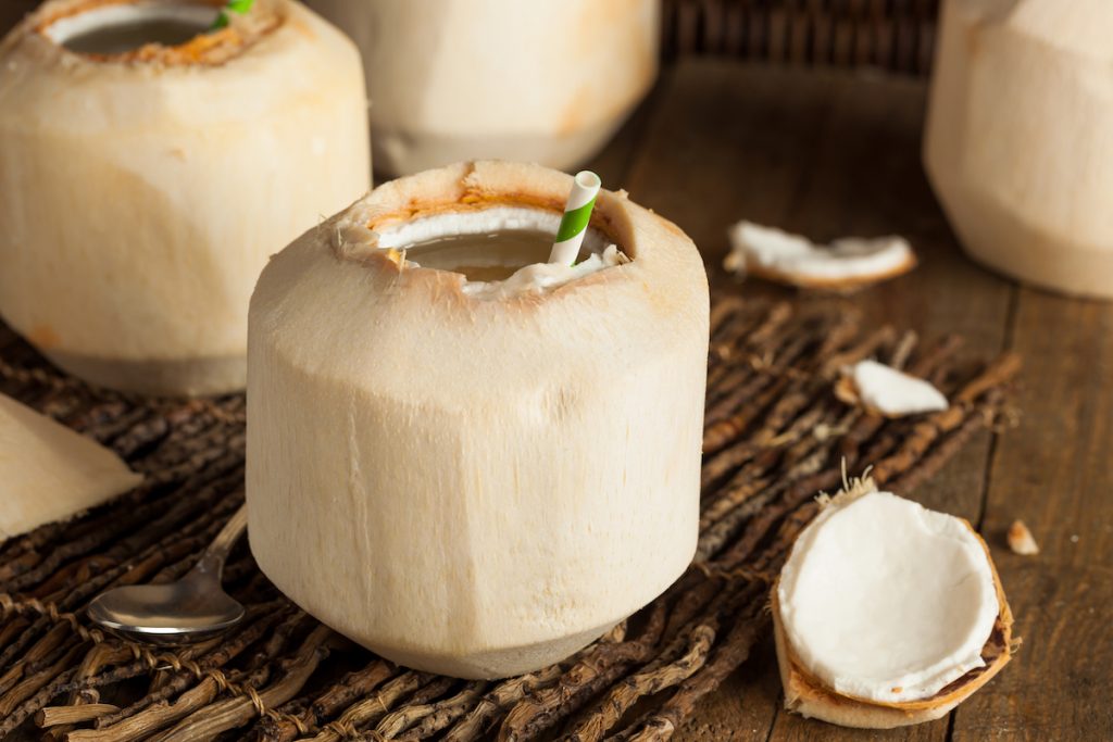 Young thai coconut open at the top with a straw in on a wooden surface
