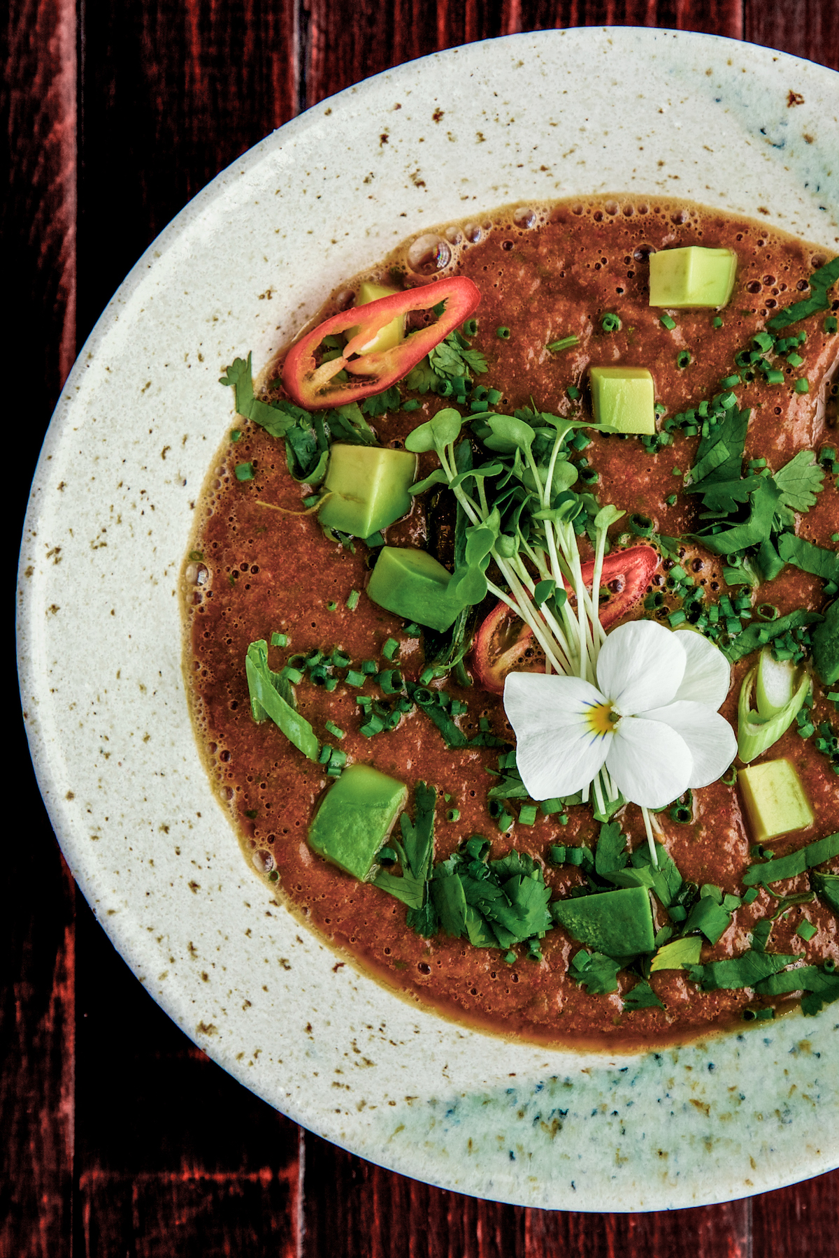 Raw Mexican tomato soup with garnish in a white bowl on a wooden bacground