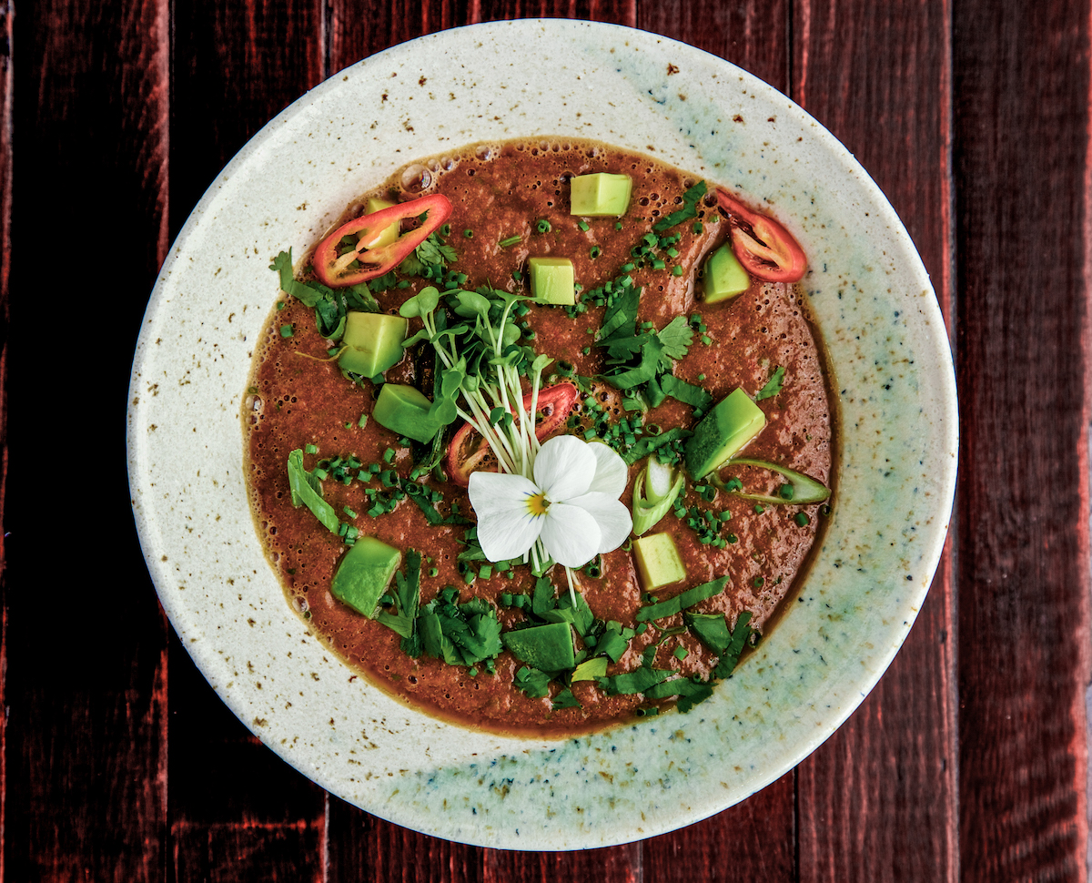 Raw Mexican tomato soup with garnish in a white bowl on a wooden bacground