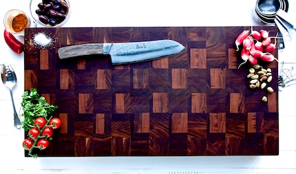 Chefs knife on a wooden chopping board with various vegetables around it