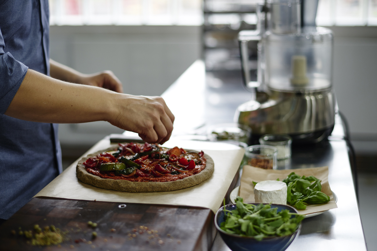 Russell James garnishing a raw pizza on a wooden chopping board