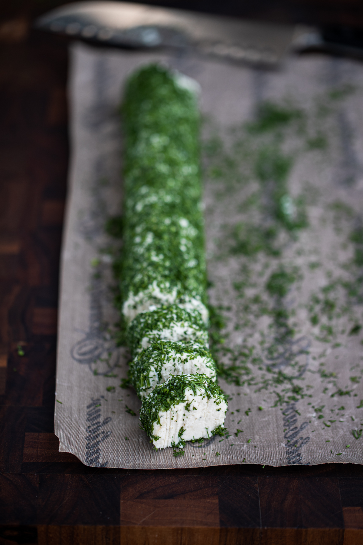 Macadamia cheese log rolled in herbs and cut into rounds on a dehydrator nonstick sheet with a knife in the background