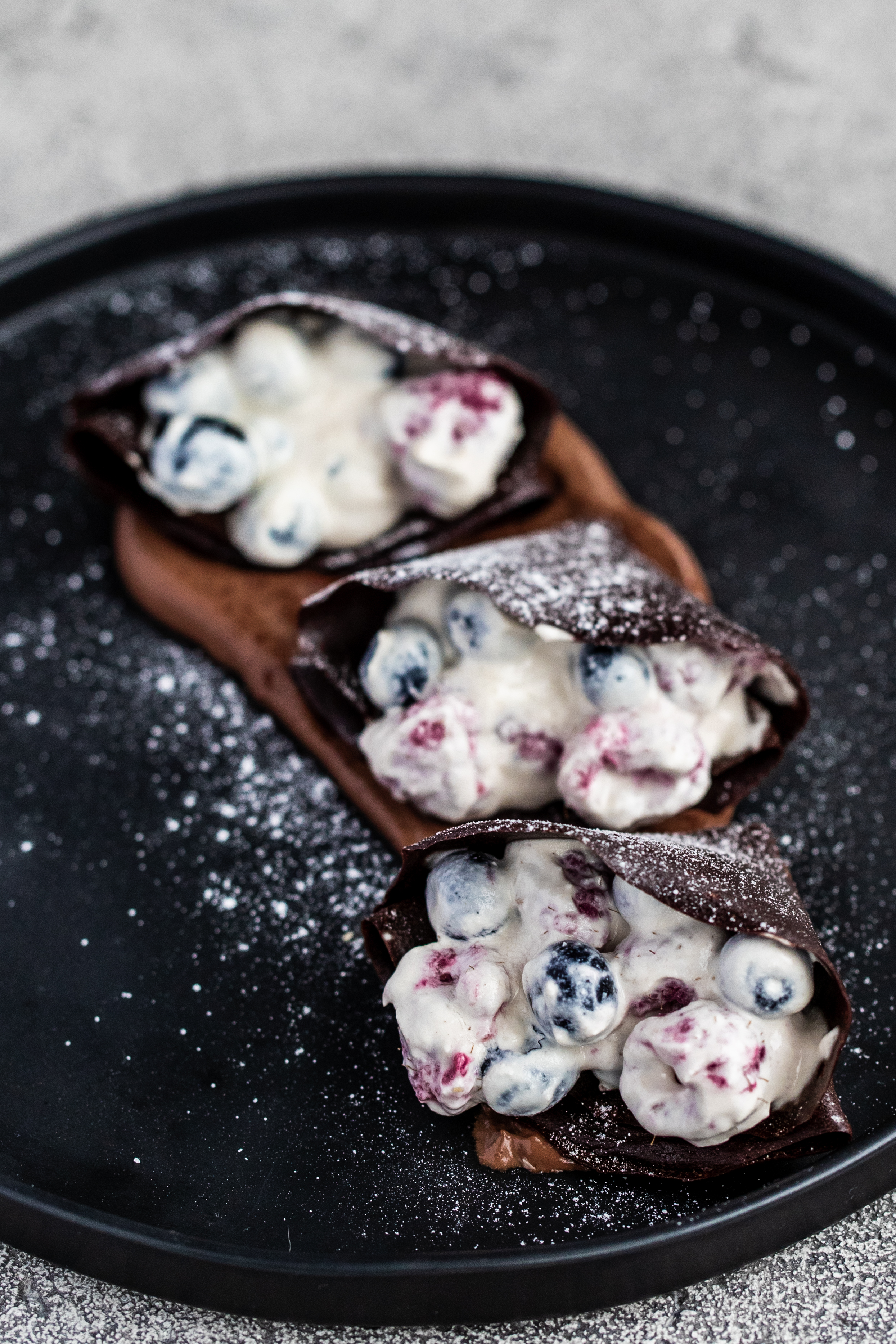 3 cacao crepes with cashew creme fraiche and chocolate sauce on a black plate