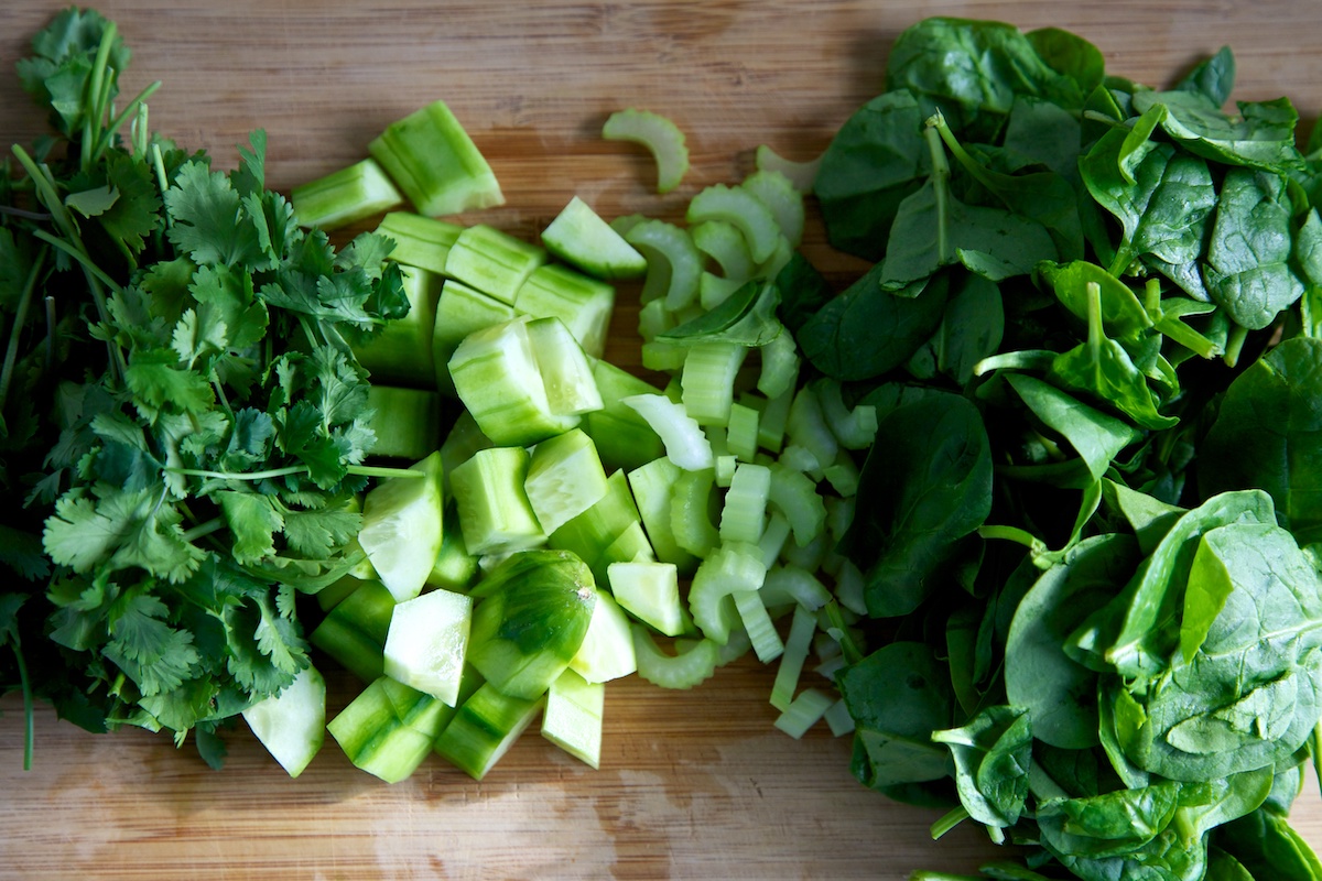 Fresh coriander, cucumber, celery and spinach on a wooden chopping board.