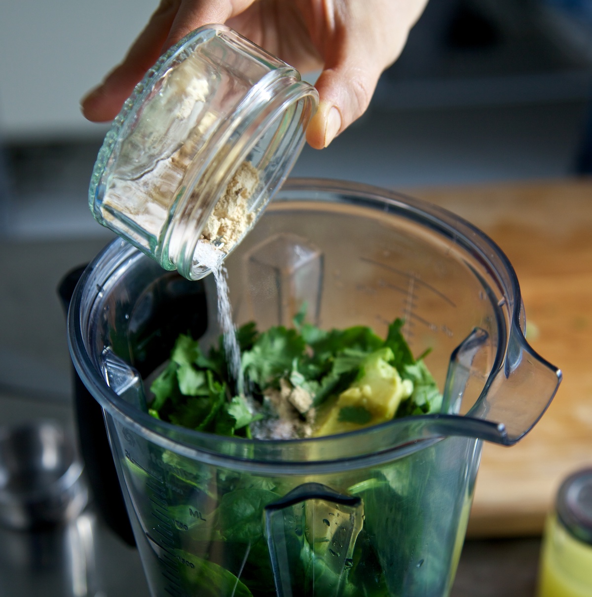 Adding spices to the Vitamix jug with the raw avocado, spinach and lime soup ingredients in