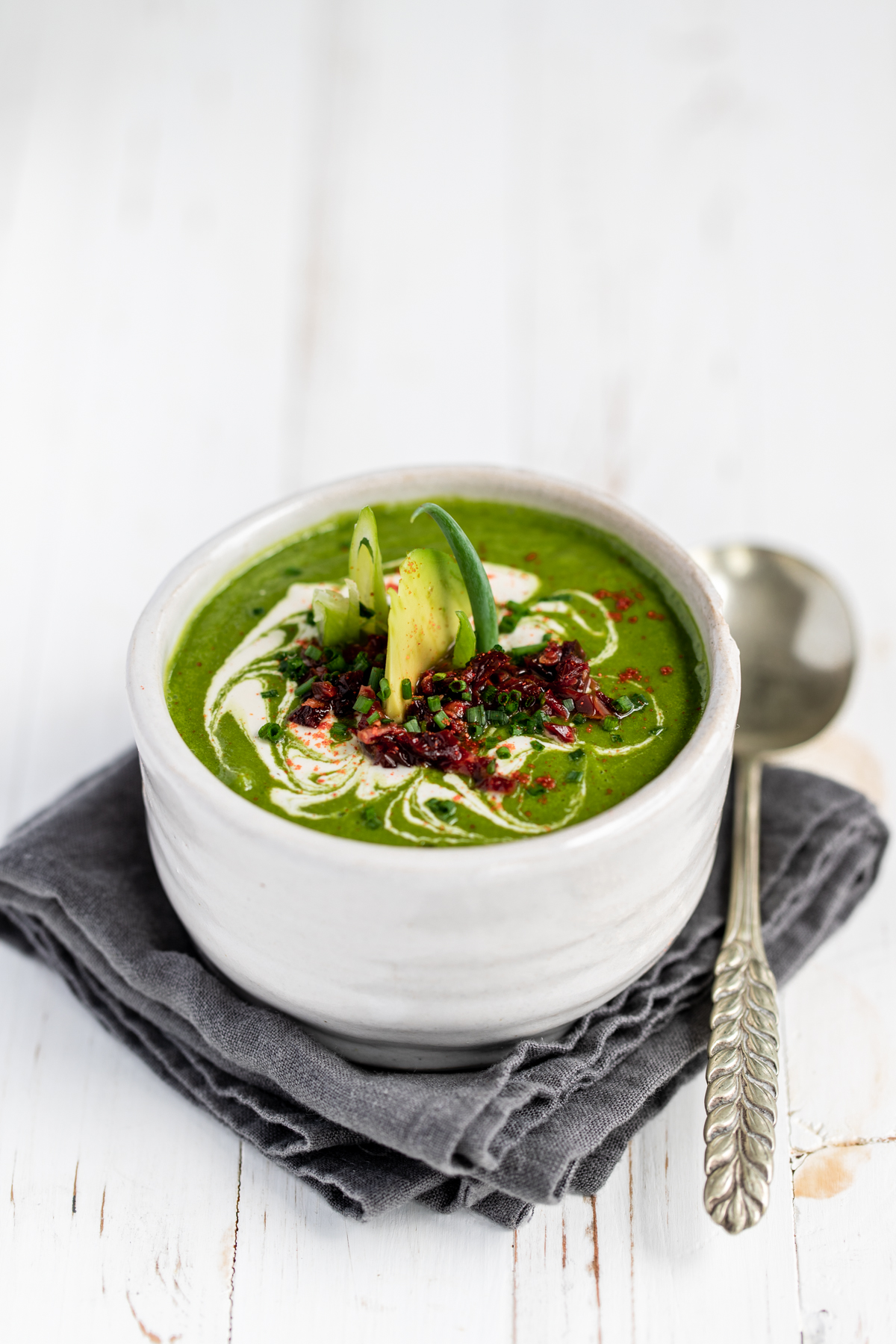 Raw avocado spinach lime soup in a white bowl on a white background